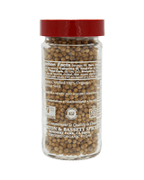 A clear glass jar with a red lid, filled with brown coriander seeds. The label displays nutrition facts and organic certification.